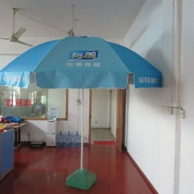 A 2.4M Oxford Beach Umbrella is sitting on a wooden floor in an office.