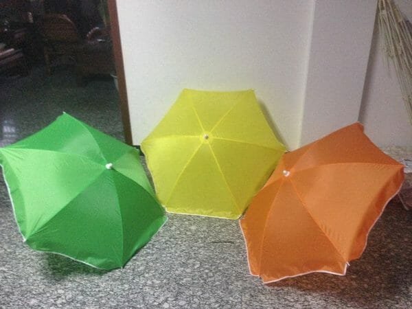 Three 1.2M Polyester Beach Umbrellas sitting on a floor in a room.