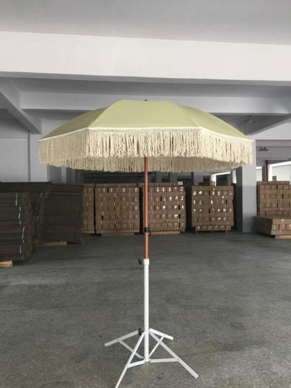 An ARDECO 1.8M Fringe 400g Polyester Green Beach Umbrella with tassels on a stand in a warehouse.