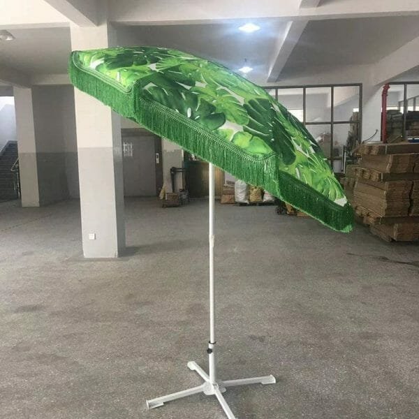 A 1.8M Fringe 400g Polyester Green Beach Umbrella on a stand in a warehouse.