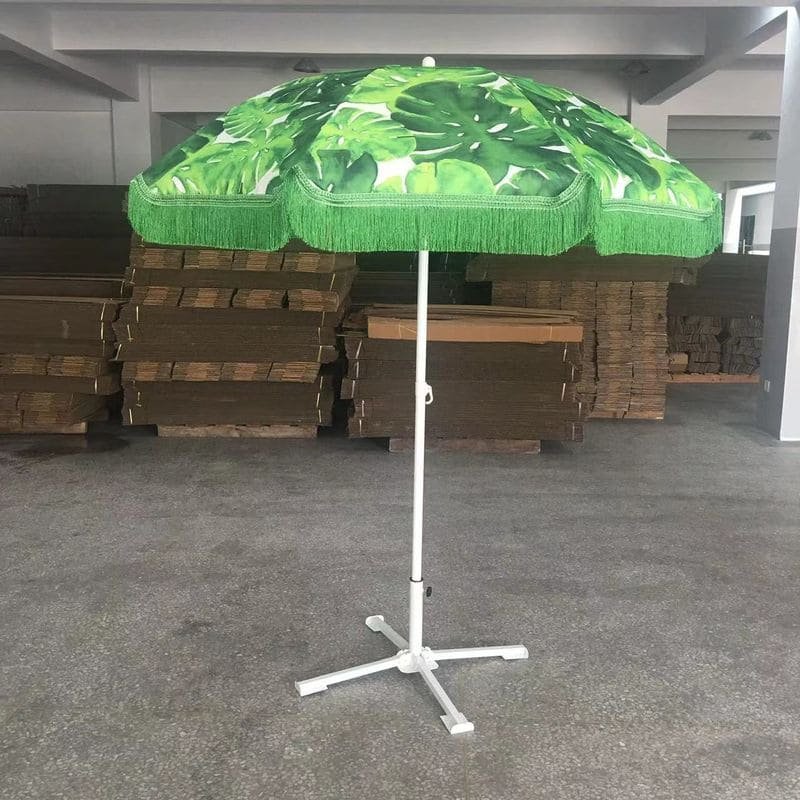A 1.8M Fringe 400g Polyester Green Beach Umbrella on a stand in a warehouse.
