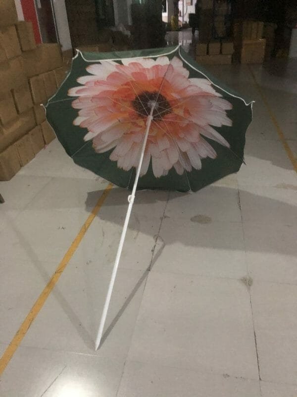 An 1.8M Polyester Black & Yellow Beach Umbrella with a flower on it sitting in a warehouse.