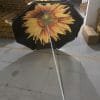 An 1.8M Polyester Black & Yellow Beach Umbrella with a sunflower on it in a warehouse.