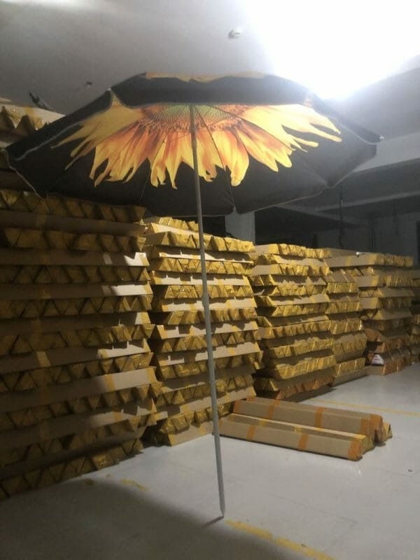 The 1.8M Polyester Black & Yellow Beach Umbrella with a sunflower on it is sitting in a warehouse.