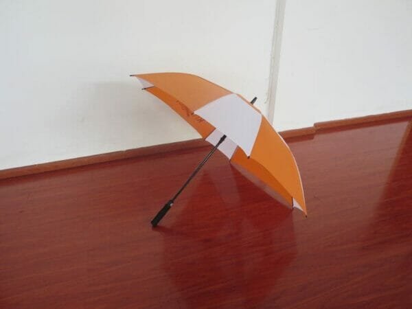 A white and orange 27inch Double Layer Golf Umbrella sitting on a wooden floor.