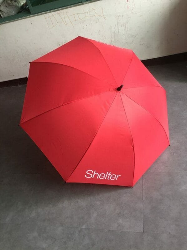 A red 30in Single Layer Auto Golf Umbrella Printed with the word shelter on it.