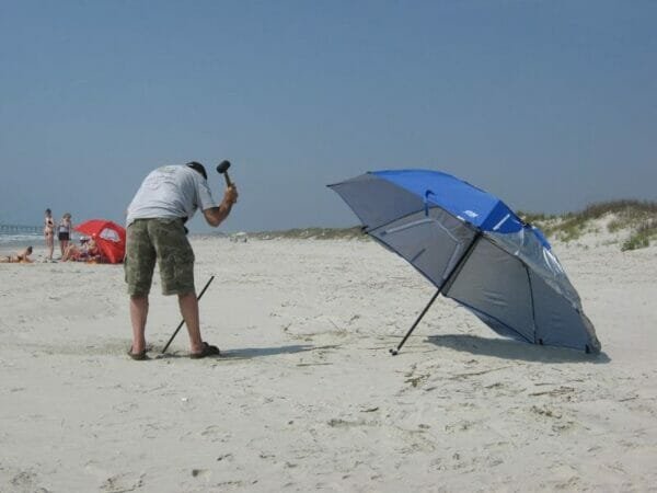 a man standing on top of a sandy beach holding a blue umbrella